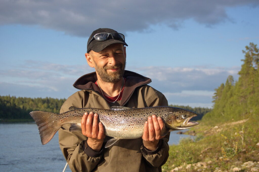 Ein gl&uuml;cklicher Angler h&auml;lt vor dem Fluss Warsuga einen gefangen Lachs.