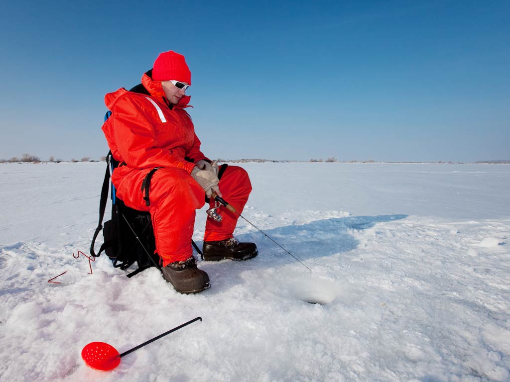 A male angler wearing all red and ice fishing on a frozen lake in New Jersey