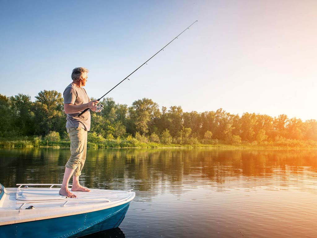 A photo featuring a barefoot angler standing on a charter boat in the shallows and casting for Snook near the shoreline