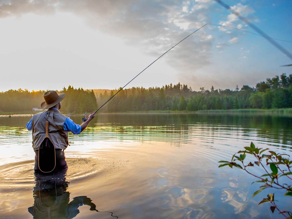 A photo featuring a wade fishing angler standing in the water and casting during the sunrise