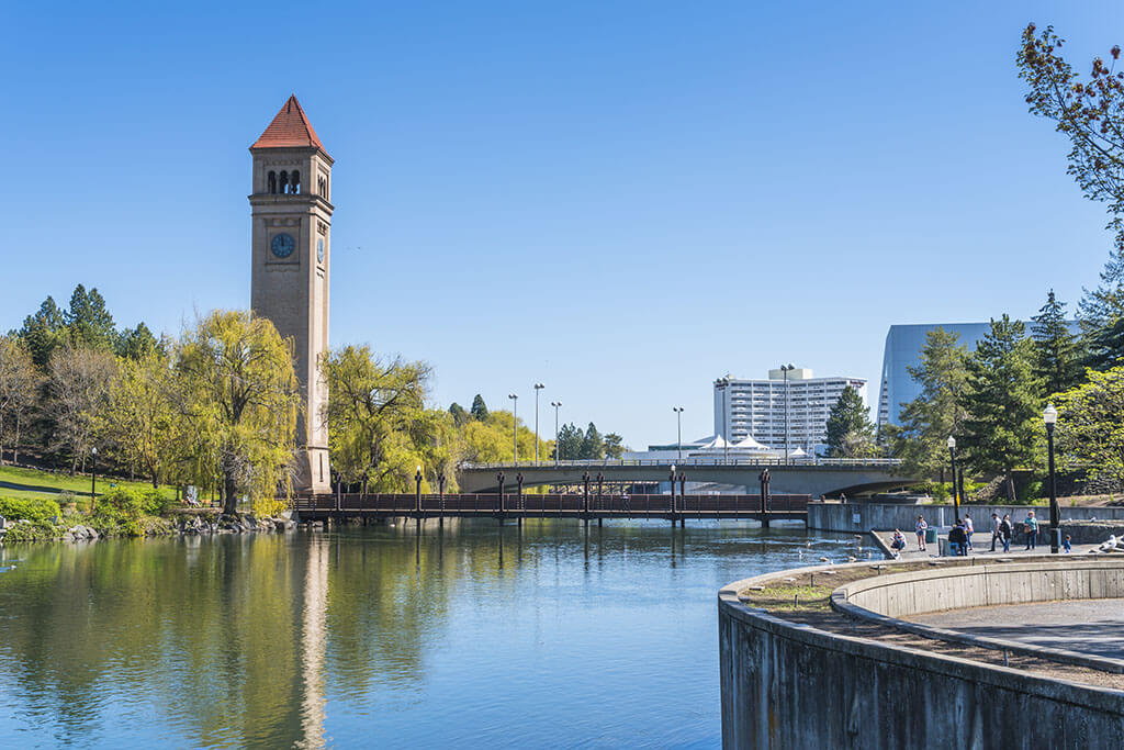 The Spokane River flowing through the center of Spokane, WA, with a clock tower rising through the trees on the left