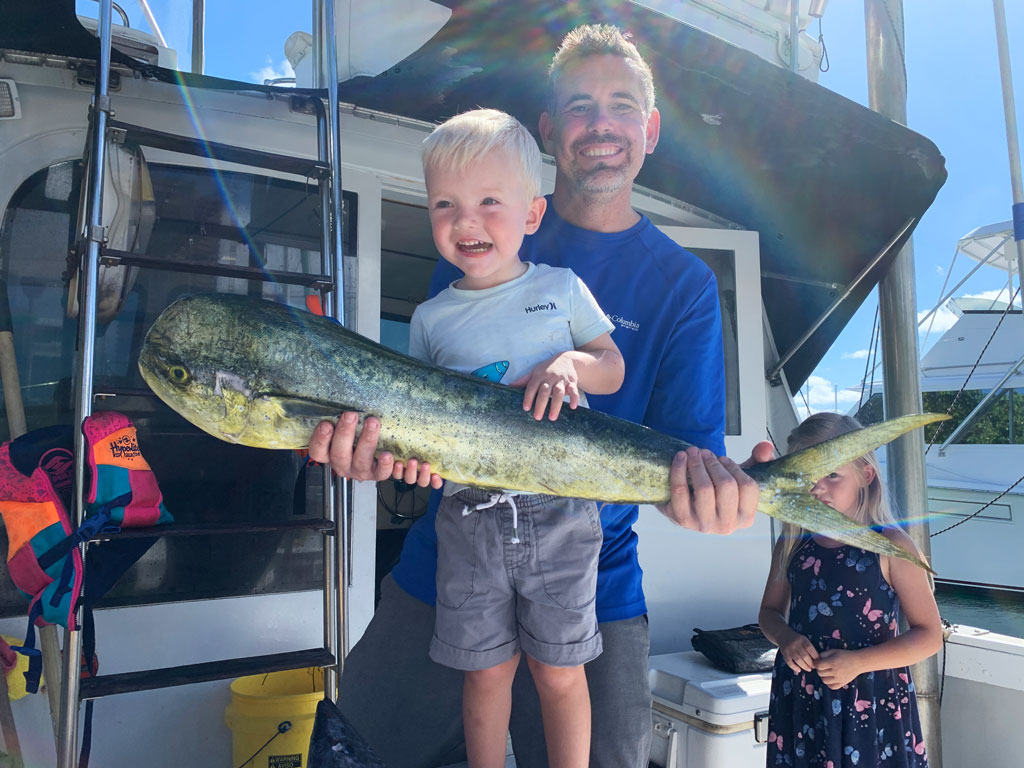 Father and son standing on a charter boat, holding a Mahi Mahi fish