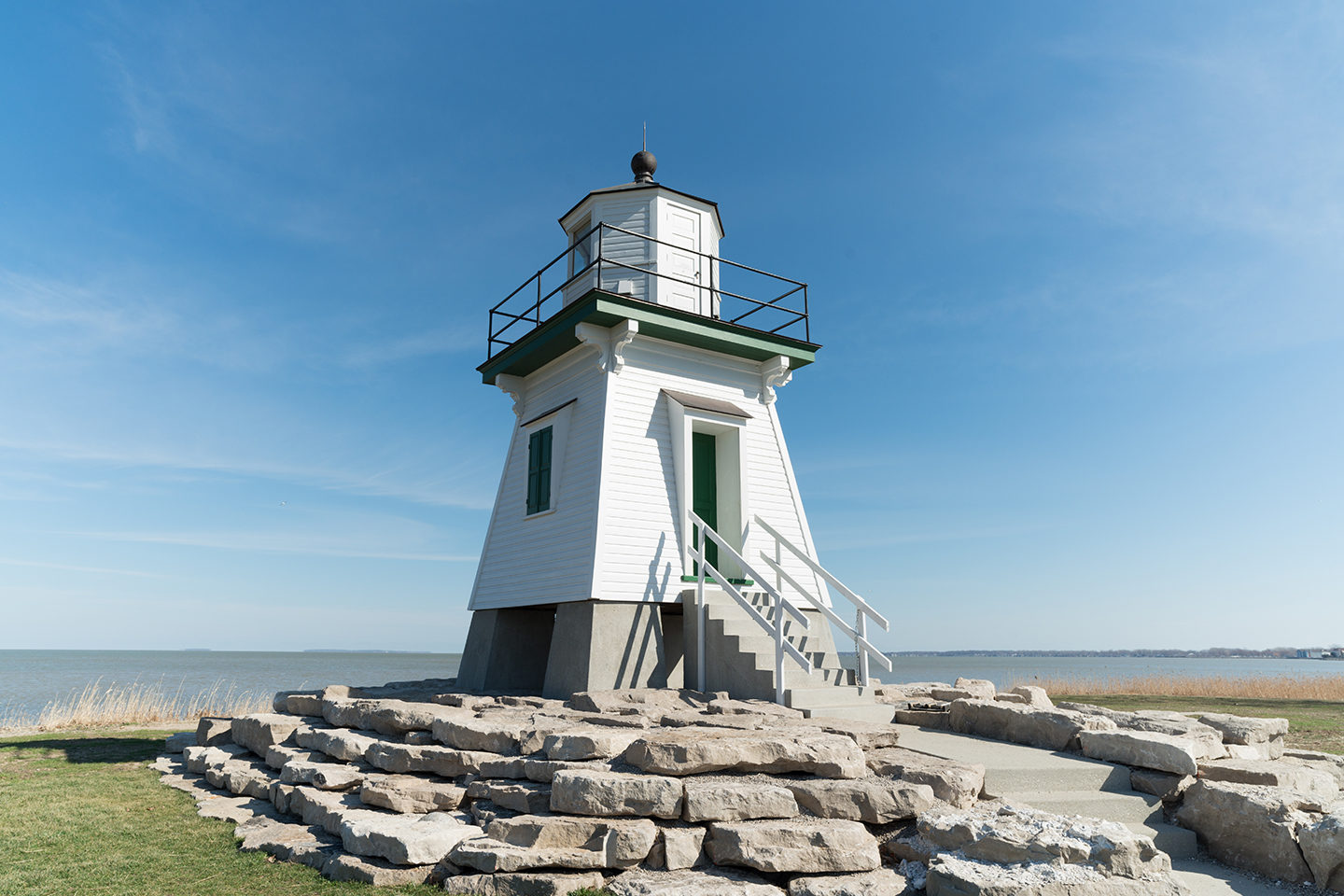 A white lighthouse in Port Clinton, one of the best summer fishing destinations on the Great Lakes, with the blue sky behind and green grass beneath it
