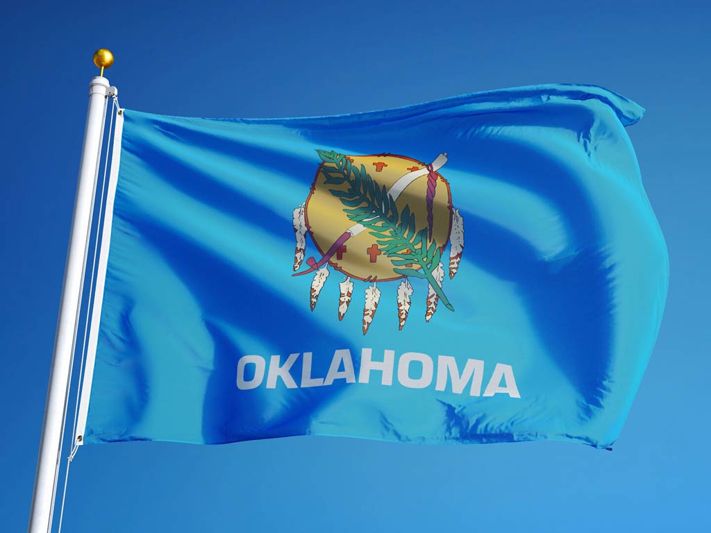 The state flag of Oklahoma flying in the wind in front of a blue sky.