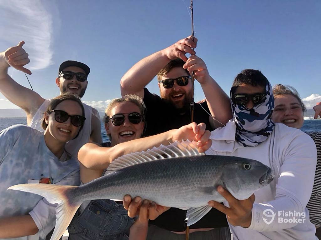 A group of anglers on a fishing boat out of Honolulu holding up a fish they caught on a clear day.