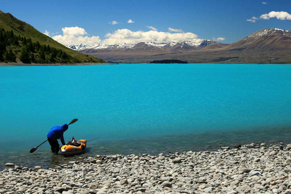 A kayaker getting ready to go out, standing on a coast of a New Zealand lake with bright blue waters