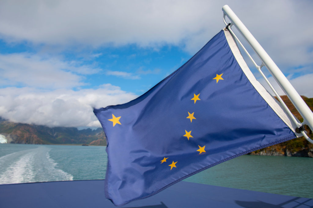 The Alaskan state flag blowing in the wind on the back of a boat heading out to sea