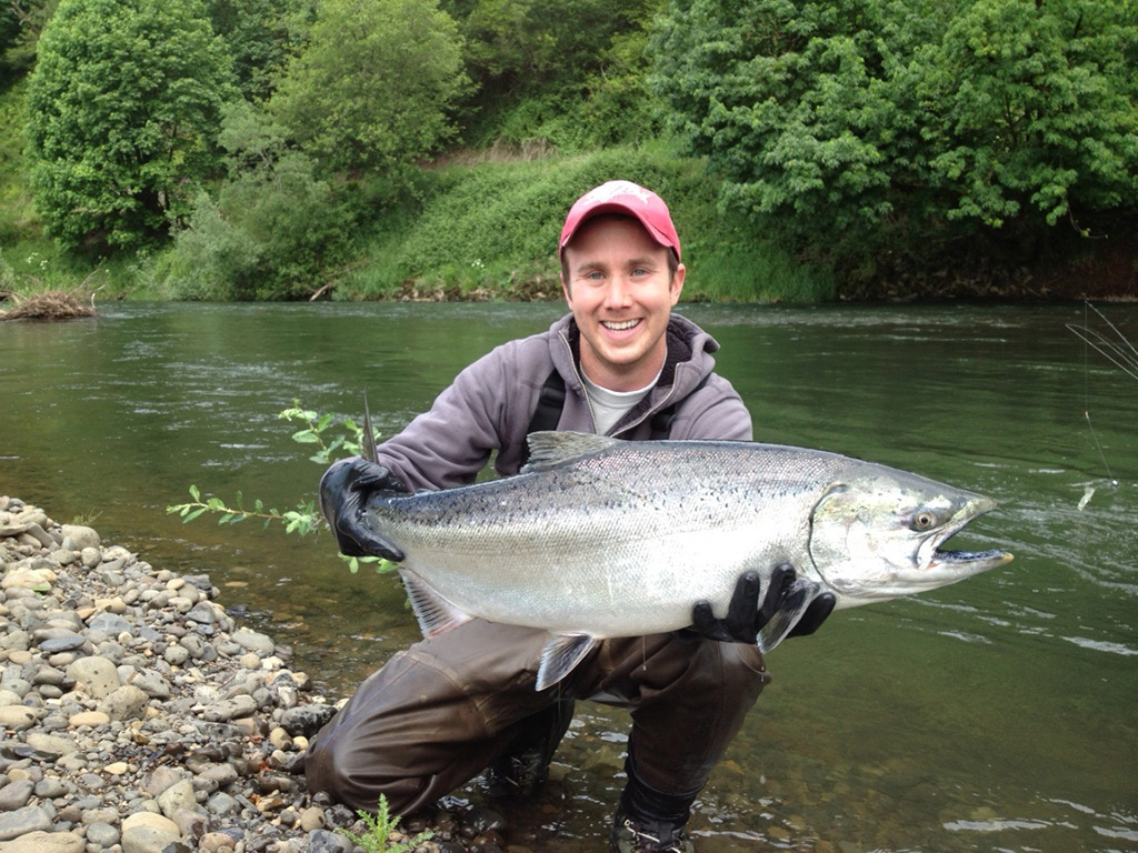 A man crouches in a river holding a large Salmon after fishing in Oregon