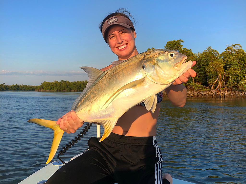 A woman in a vizer holding a large inshore fish on the calm waters of South Florida at sunset. 