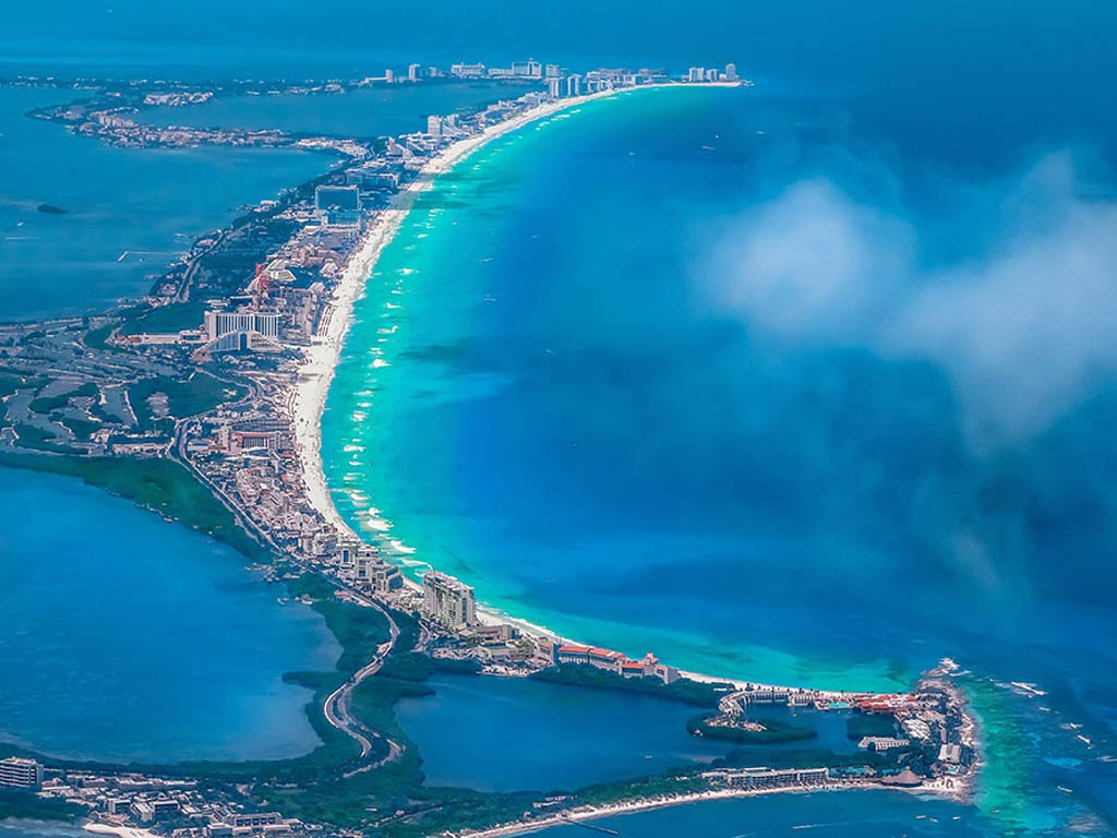 An aerial view of Cancún with a beach and the ocean on the right hand side and bays on the left