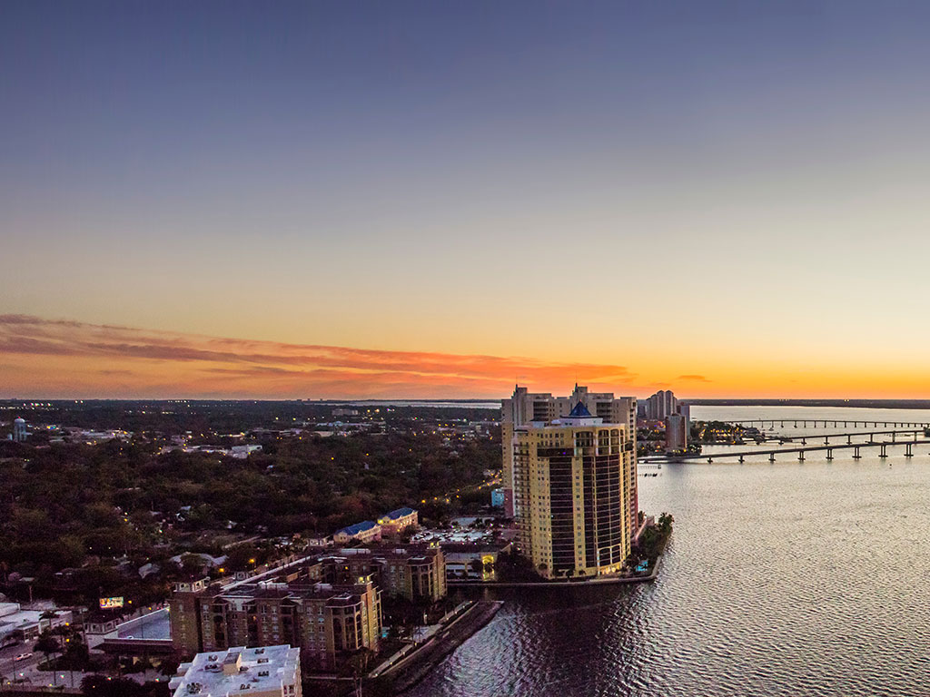 An aerial view of Fort Myers at dusk, with the ocean on the right-hand side and bridges in the distance