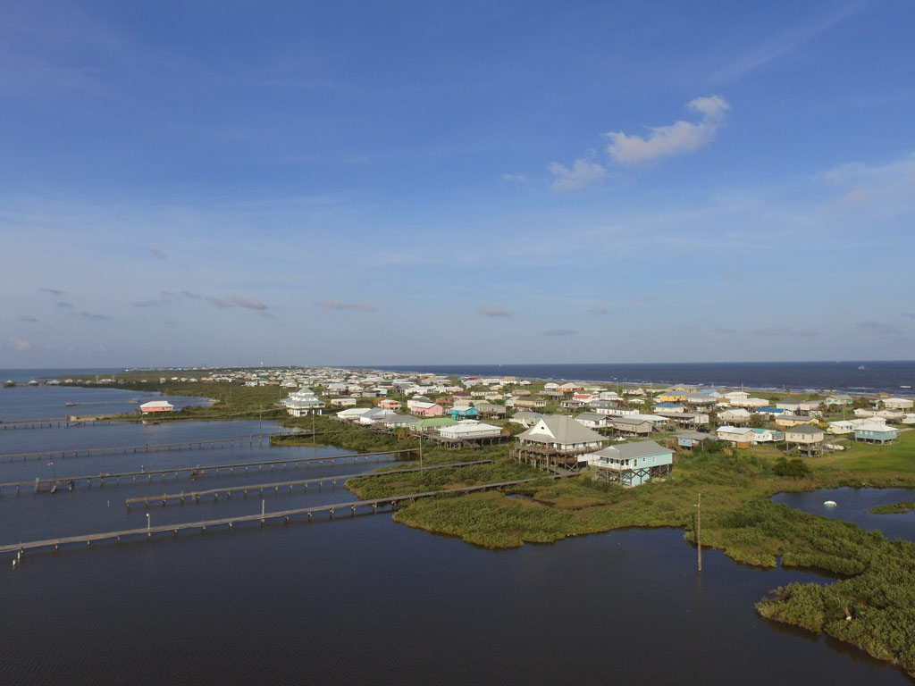 An aerial shot of Grand Isle, Louisiana, on a clear day, with the shallow waters visible in the foreground and houses of the town in the distance