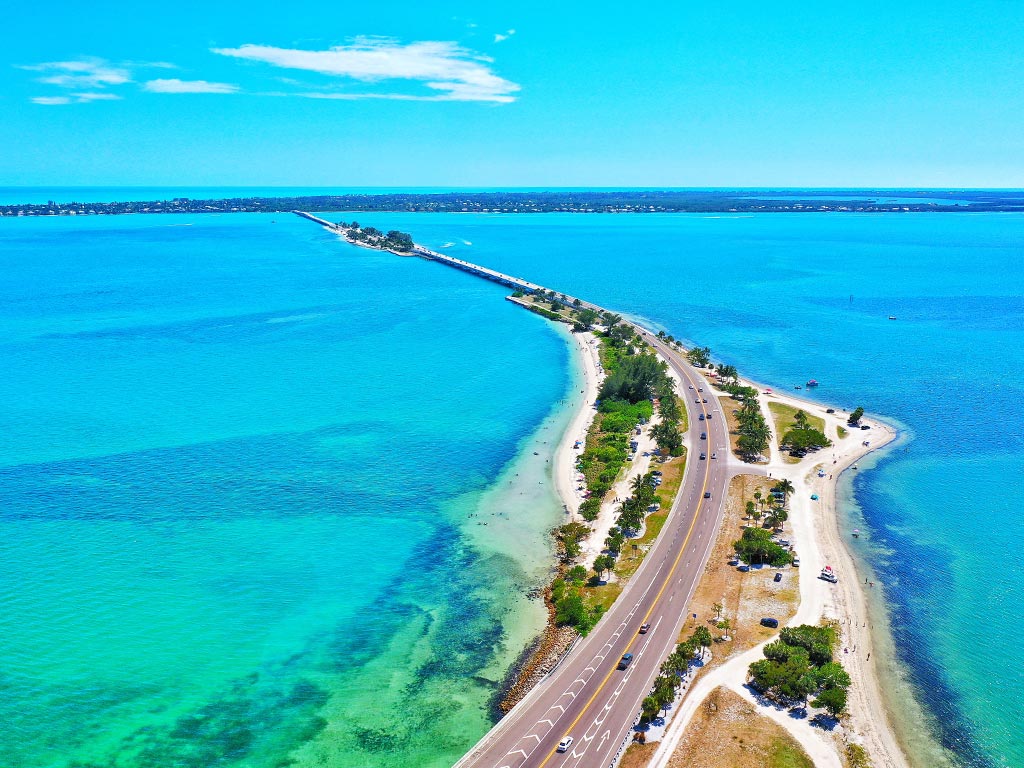 An aerial view of the Sanibel Causeway and several cars surrounded by turquoise waters and sandy beaches