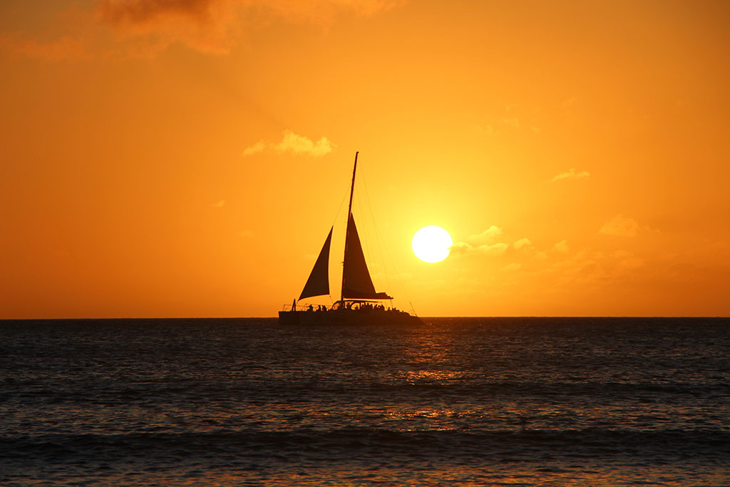 A silouhette of a boat is visible against the sunset in Aruba