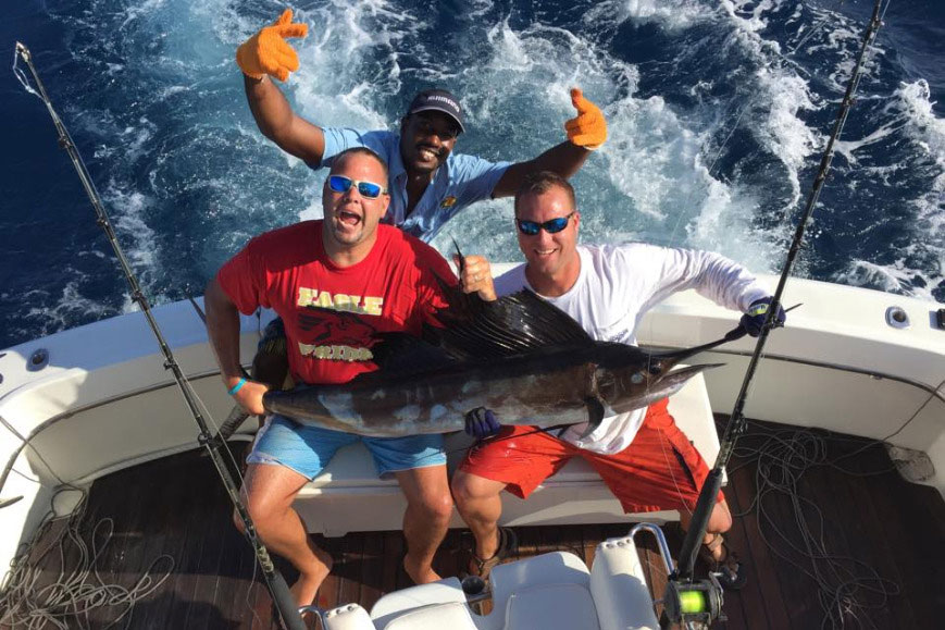 Three anglers celebrate catching a Sailfish aboard an Aruba deep sea fishing charter