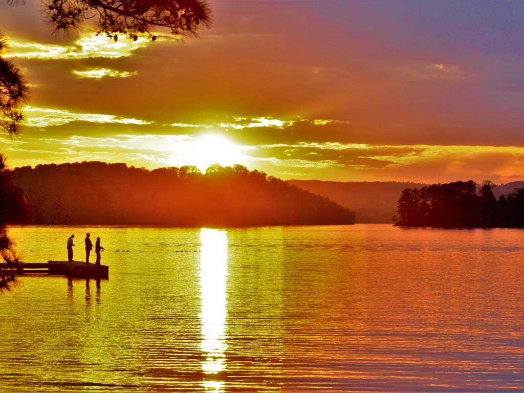 Three anglers fishing from a pier at sunset on Lake Guntersville.