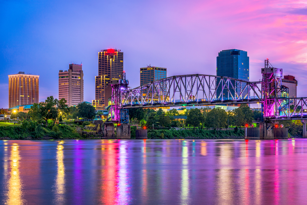 A view of Little Rock's skyline at night, lit up with the water in the foreground