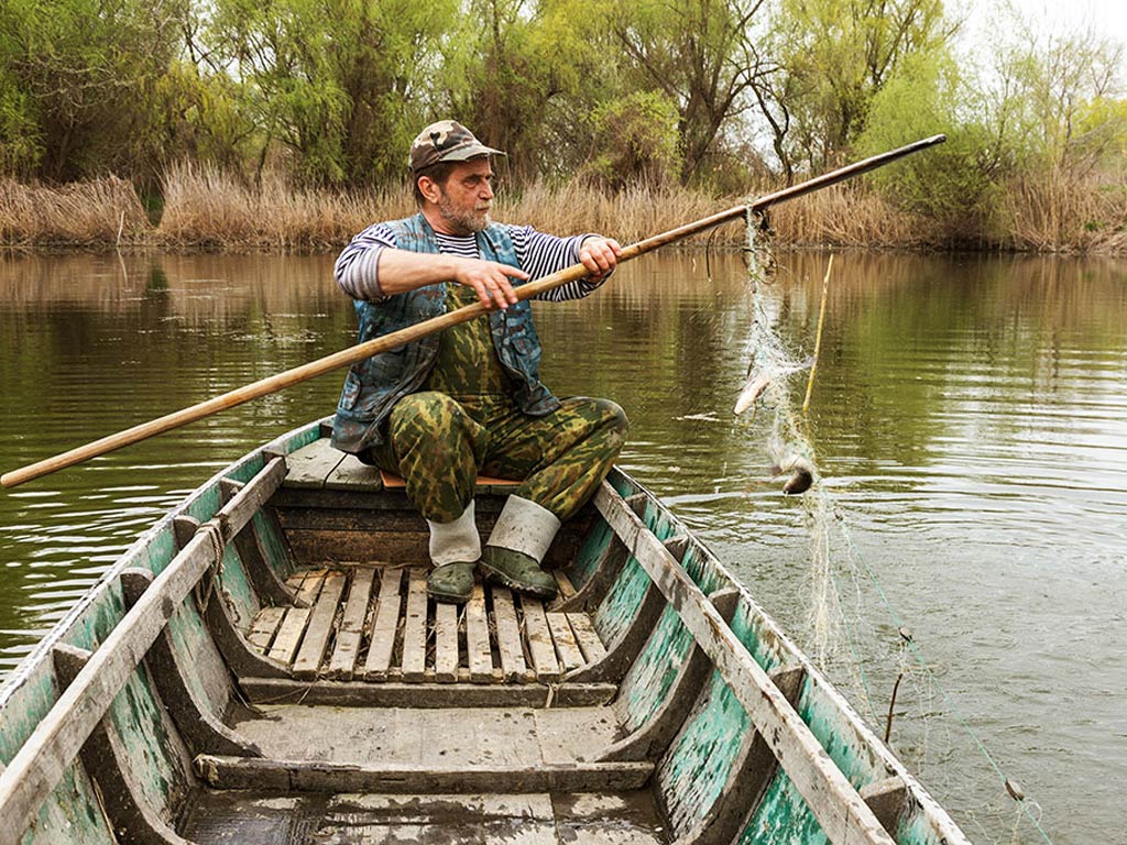 An elderly angler on a river inspects his wooden gear before fishing