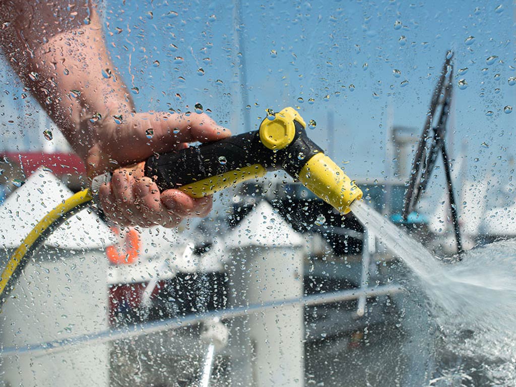 A hose pipe sprays a boat with a wet window in the foreground