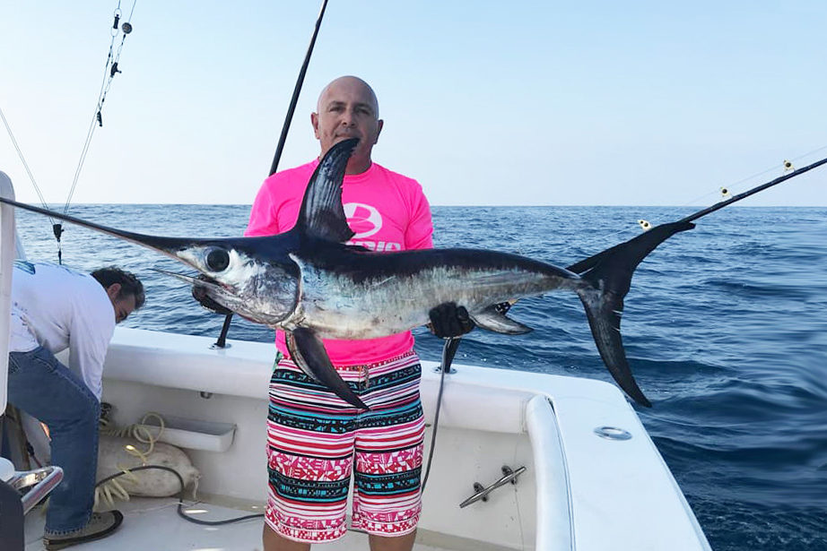 An angler holding a juvenile Swordfish on a fishing boat