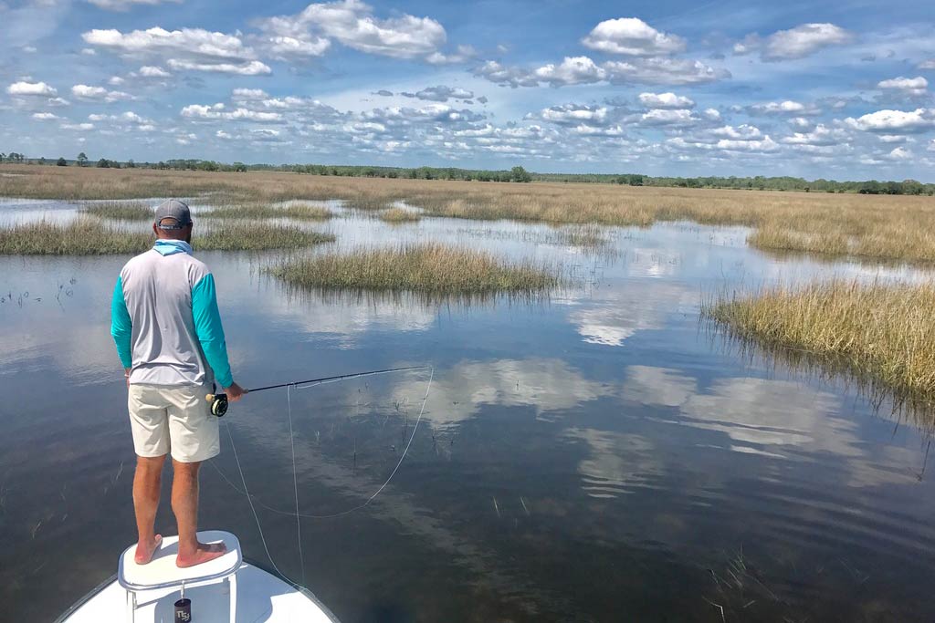 A stunning view of an angler standing on a charter boat and facing the flats while getting ready to fly fish during a sunny day