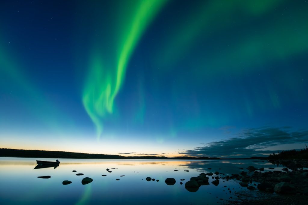 Bands of curvy aurora borealis appear over a northern rocky lake, Northern Territories, Canada.