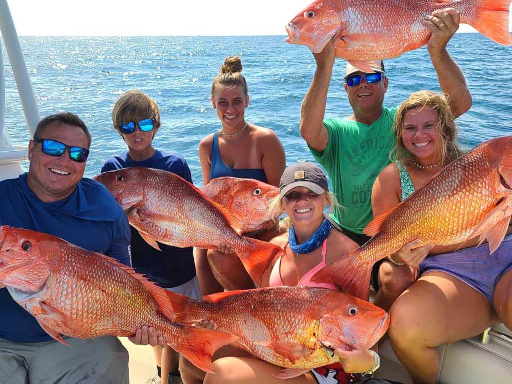 A group of anglers standing on a fishing boat, each holding a big Red Snapper