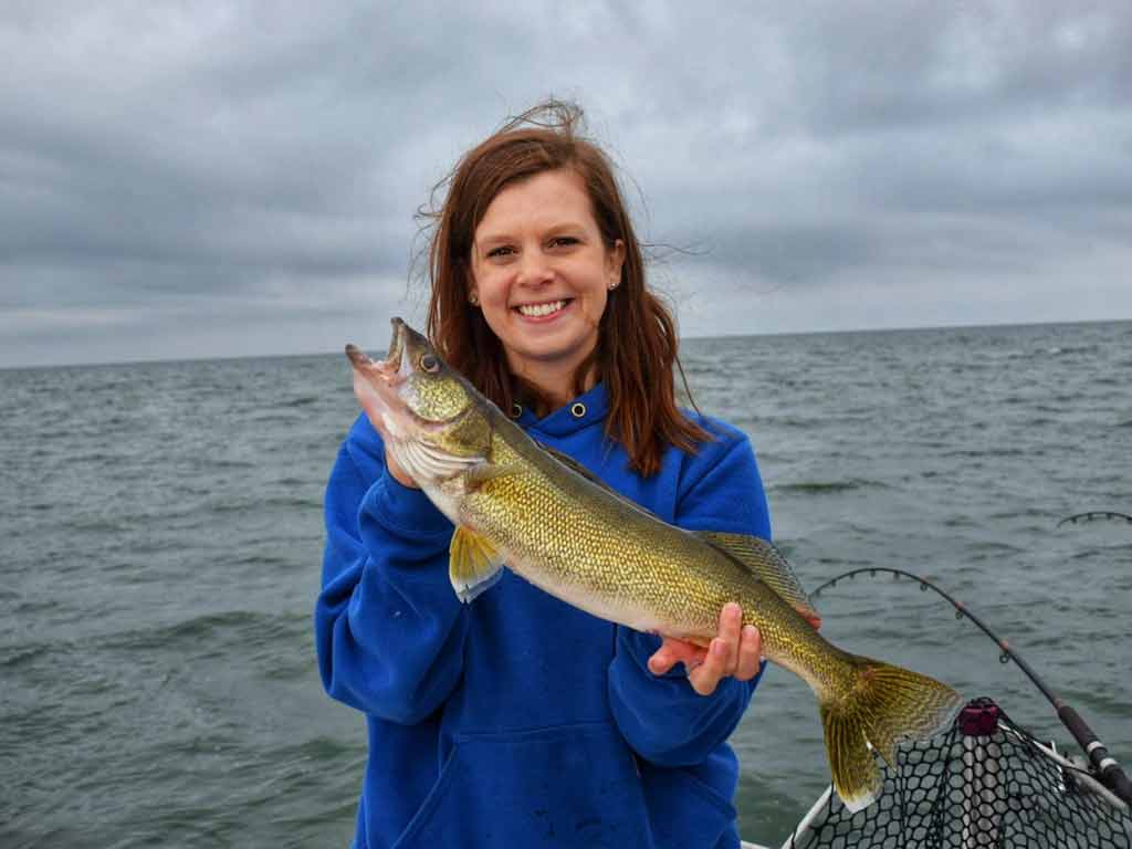 A happy woman holding her Walleye catch with both hands on a cloudy day on the water