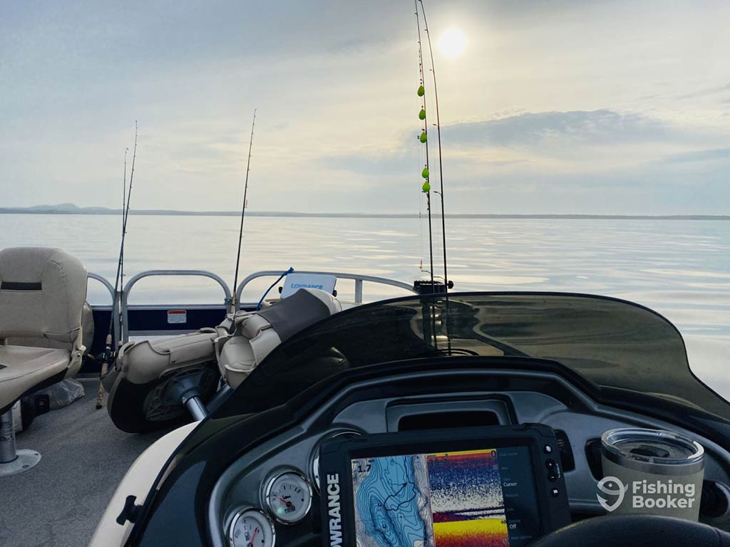 A view across a console of a fishing charter in Maine, looking towards calm waters, with a fishfinder and some fishing rods visible in the foreground