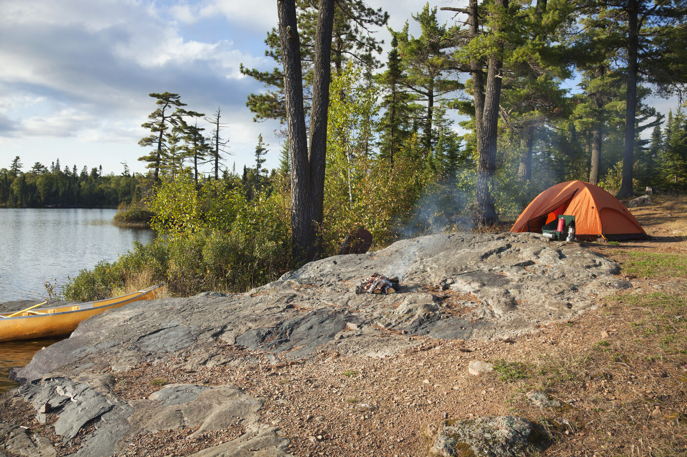 A campsite set up next to a body of water with a canoe resting on the bank