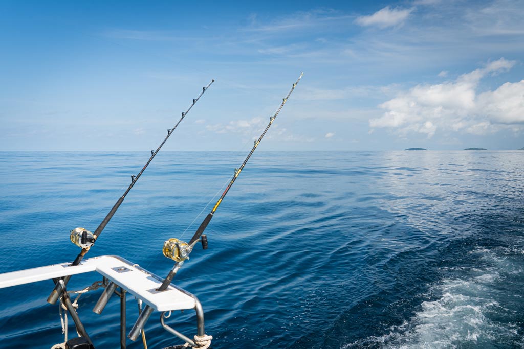 A view of two trolling rods over the side of a fishing boat on a clear day on the open waters of the ocean