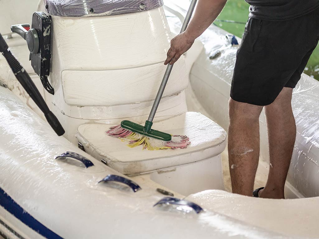 A man cleans his boat with brush and pressure water system at garage.