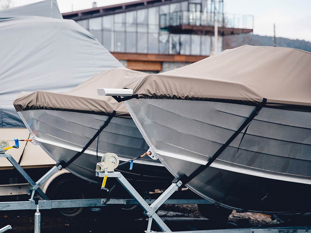 Two boats on land with canvas covers on top.