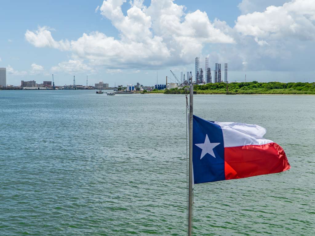 The flag of Texas in the wind flying in front of Galveston Bay and posing against the water and shoreline in the background