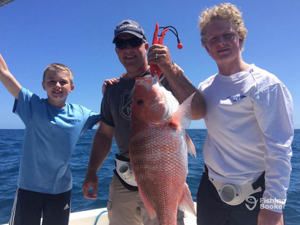 Three people proudly display a large Red Snapper on their boat after a rewarding day of deep sea fishing in Clearwater under the clear blue sky