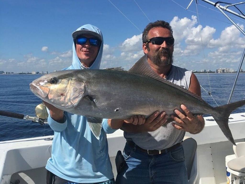 Two fishermen on a boat, holding a big Amberjack.