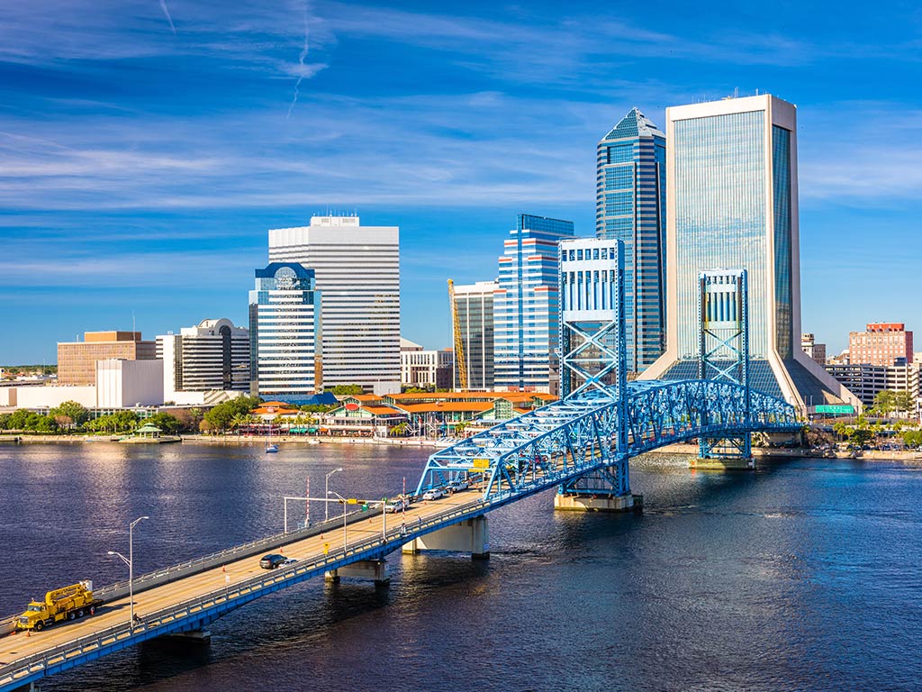 An aerial view of Jacksonville in Florida featuring skyscrapers, office buildings, bridge, and the river on a bright and sunny day
