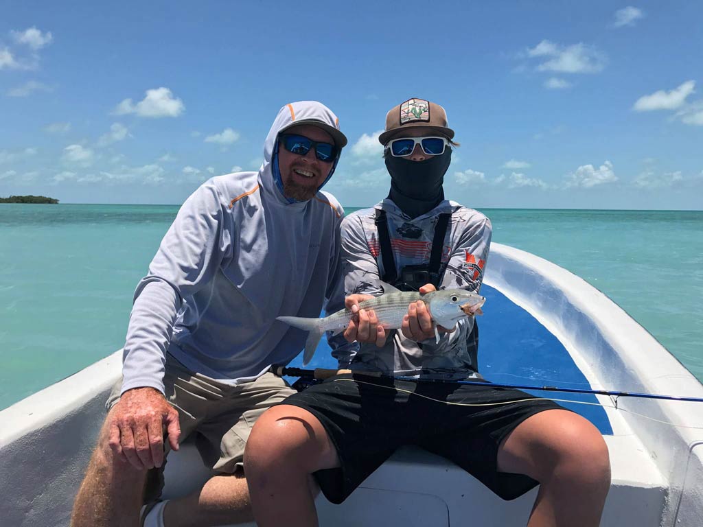 A photo featuring two anglers while sitting on a charter boat and holding a Permit they caught fly fishing in Belize