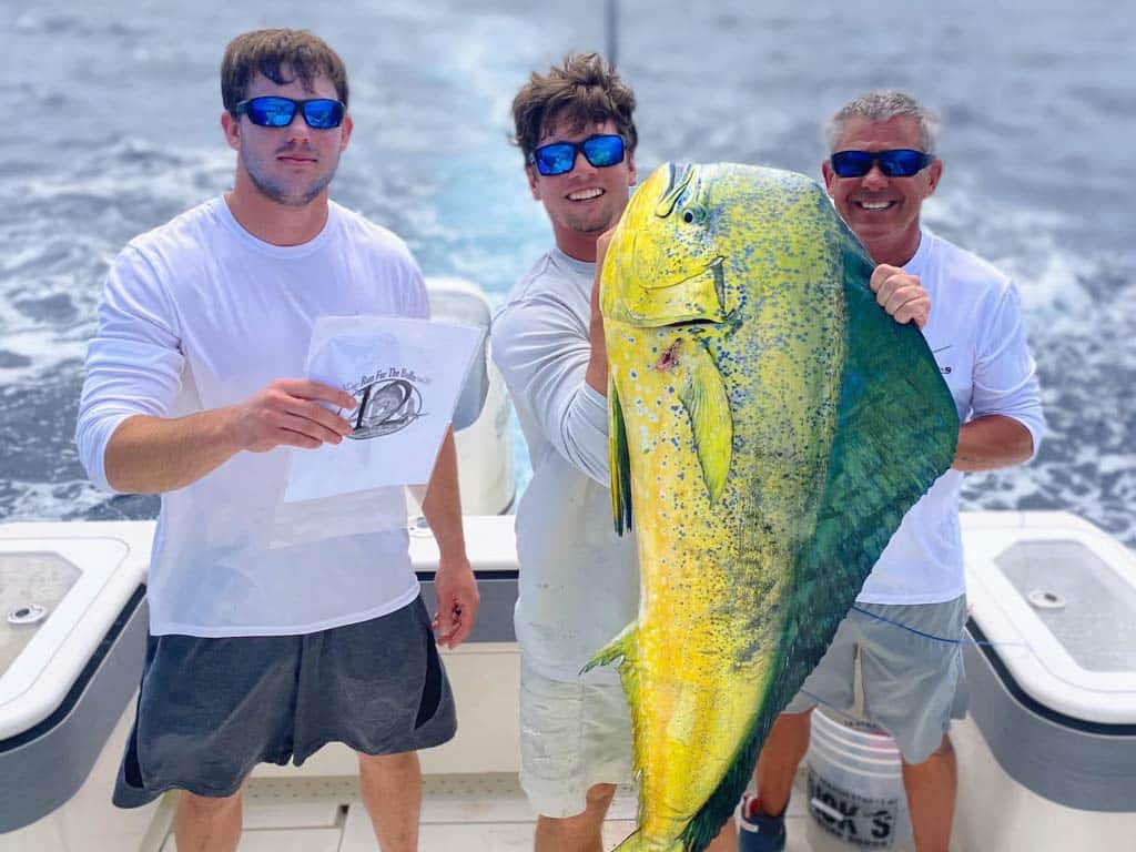 A trio of anglers posing proudly on a charter boat with a huge Mahi Mahi caught fishing offshore from Tybee Island.