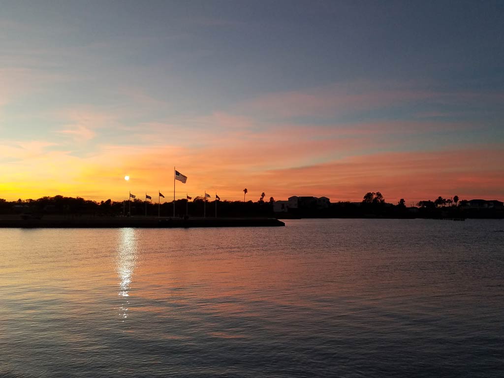 A sunset view of flags, water, and trees in Port Lavaca