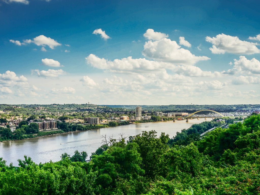 The Ohio River from a hill in Kentucky with blue sky and clouds and surrounding thick and lush greenery