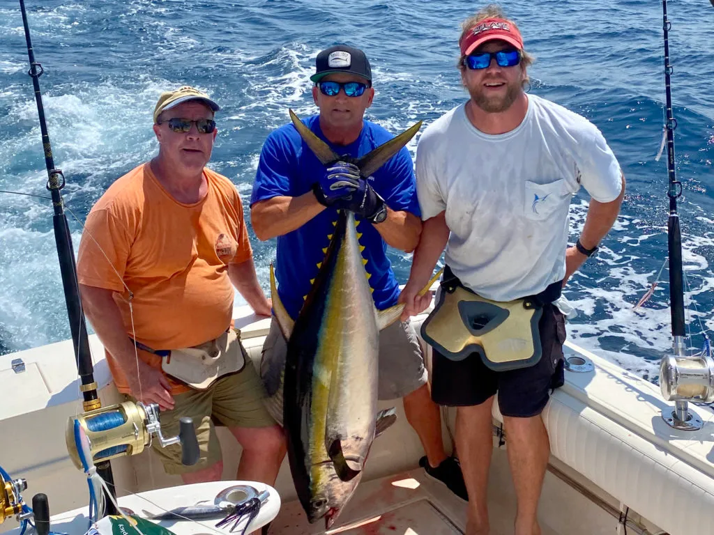 Three anglers on a boat off the coast of Virginia Beach, one of them holding a freshly caught Tuna