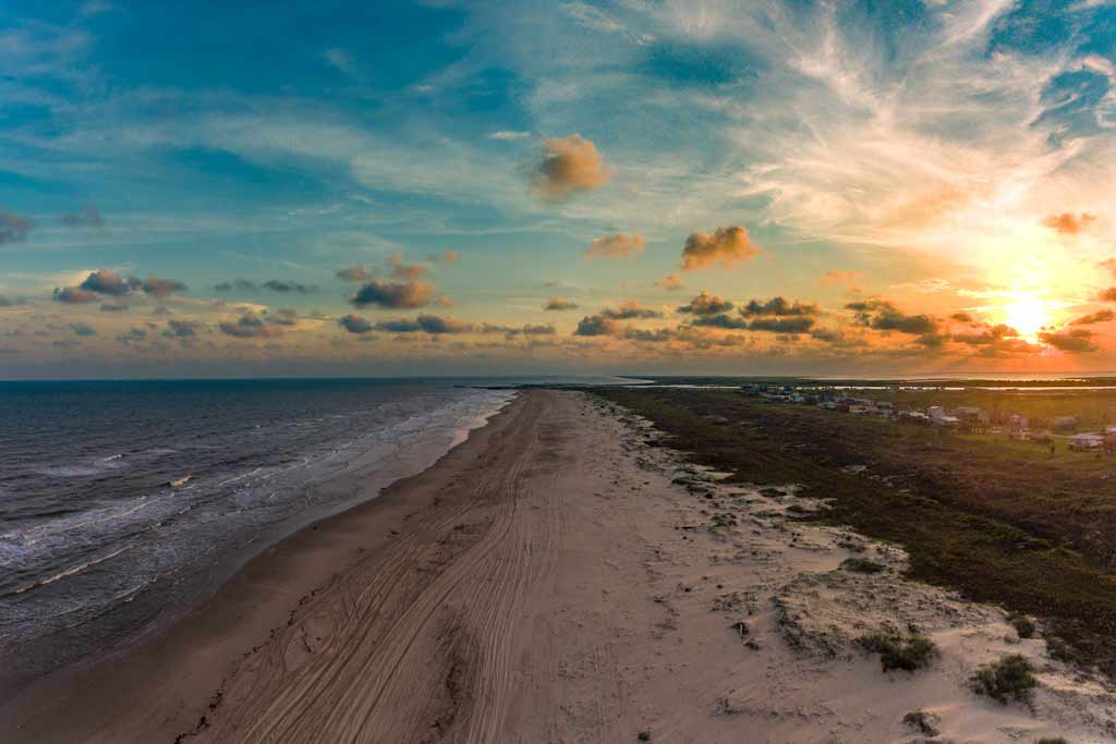 A sandy shore of Matagorda Bay at sunset with the ocean on the left of the image