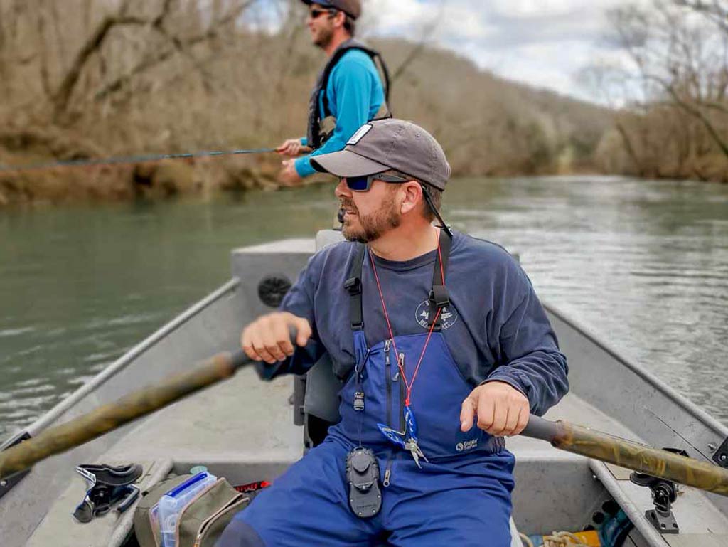 A charter captain rowing his boat and an angler standing behind him