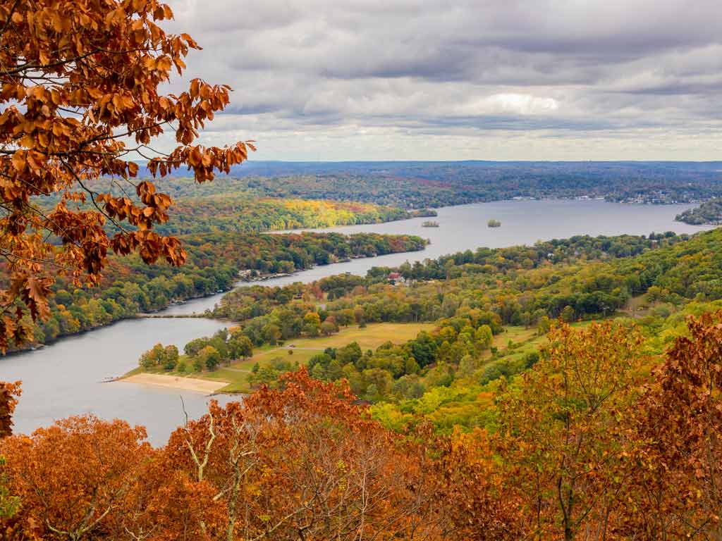 A distant view of Candlewood Lake and the surrounding fall foliage on a cloudy day.