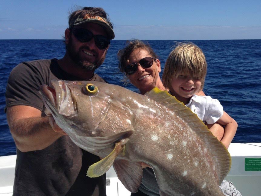 Three anglers, a male, a female, and a child, all holding a freshly-caught Grouper while standing on a charter fishing boat in Miami Beach, Florida