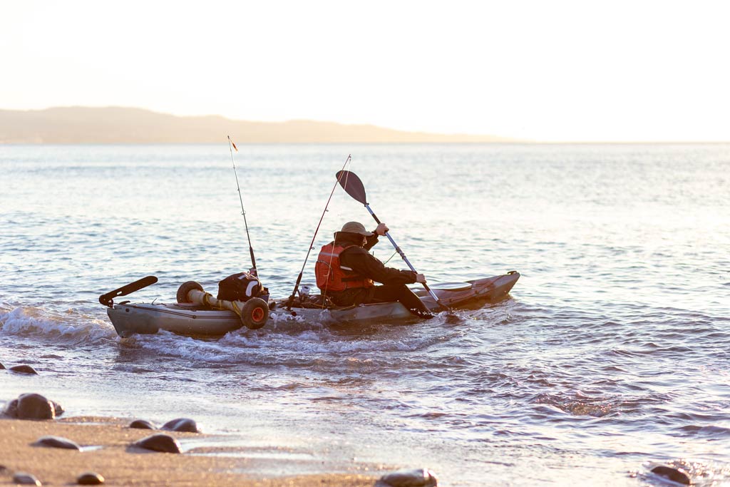 A kayak fisherman launching from a beach in his kayak on a sunny day