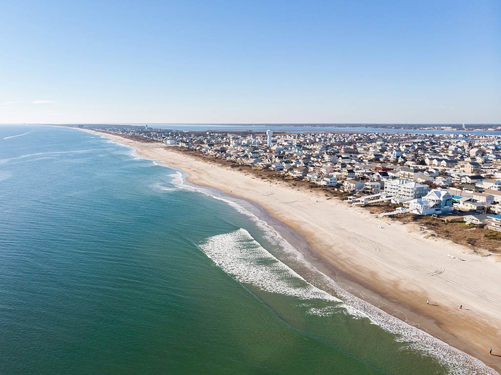An aerial view of the beach and town in Morehead City, North Carolina on a bright summer's day, with the town and the beach on the right of the image and the ocean on the left