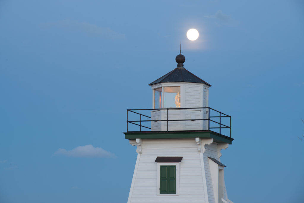 A close-up view of Port Clinton Lighthouse by Lake Erie with the Moon behind it