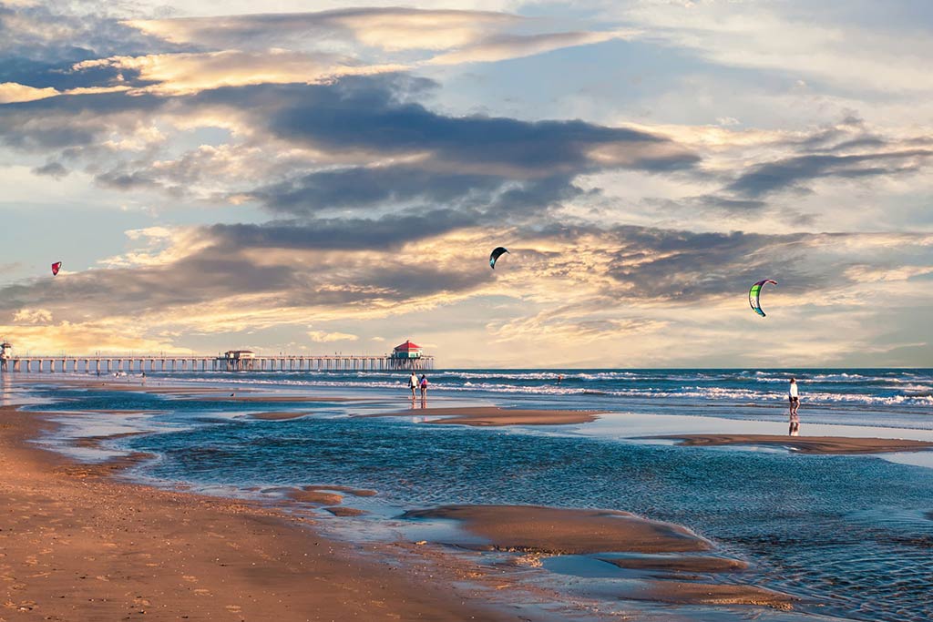 A view along the beach in Mission Bay, CA, towards the sea, with people fling kites and some impressive clouds visible near sunset